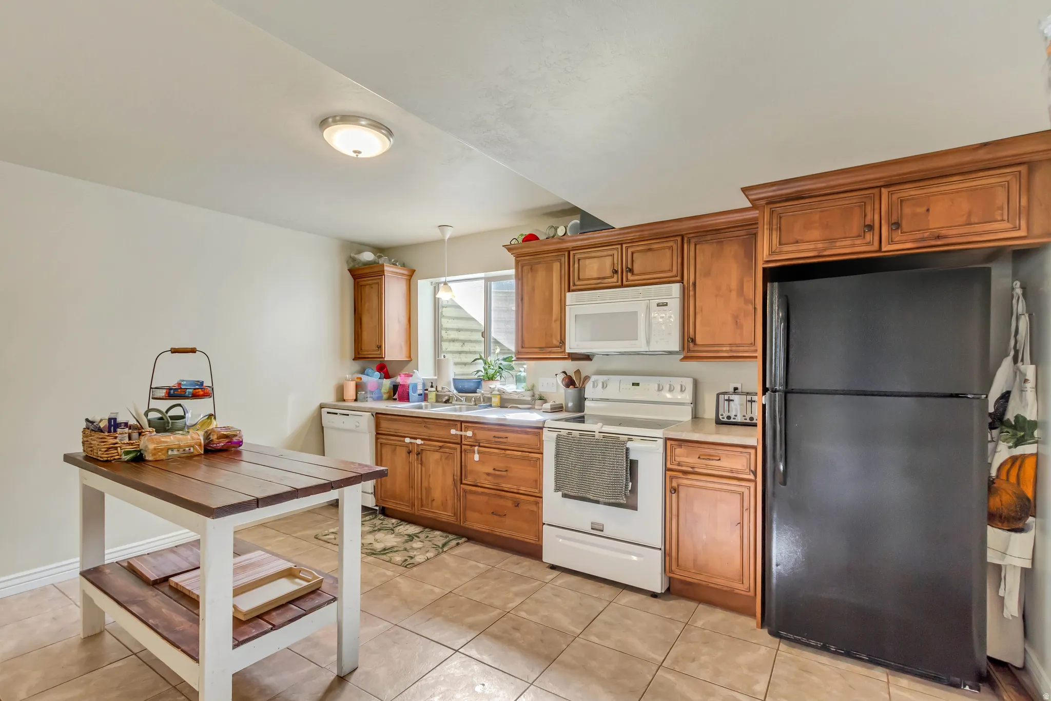 Kitchen featuring warm wood cabinetry, white appliances, a built-in microwave, and tile flooring