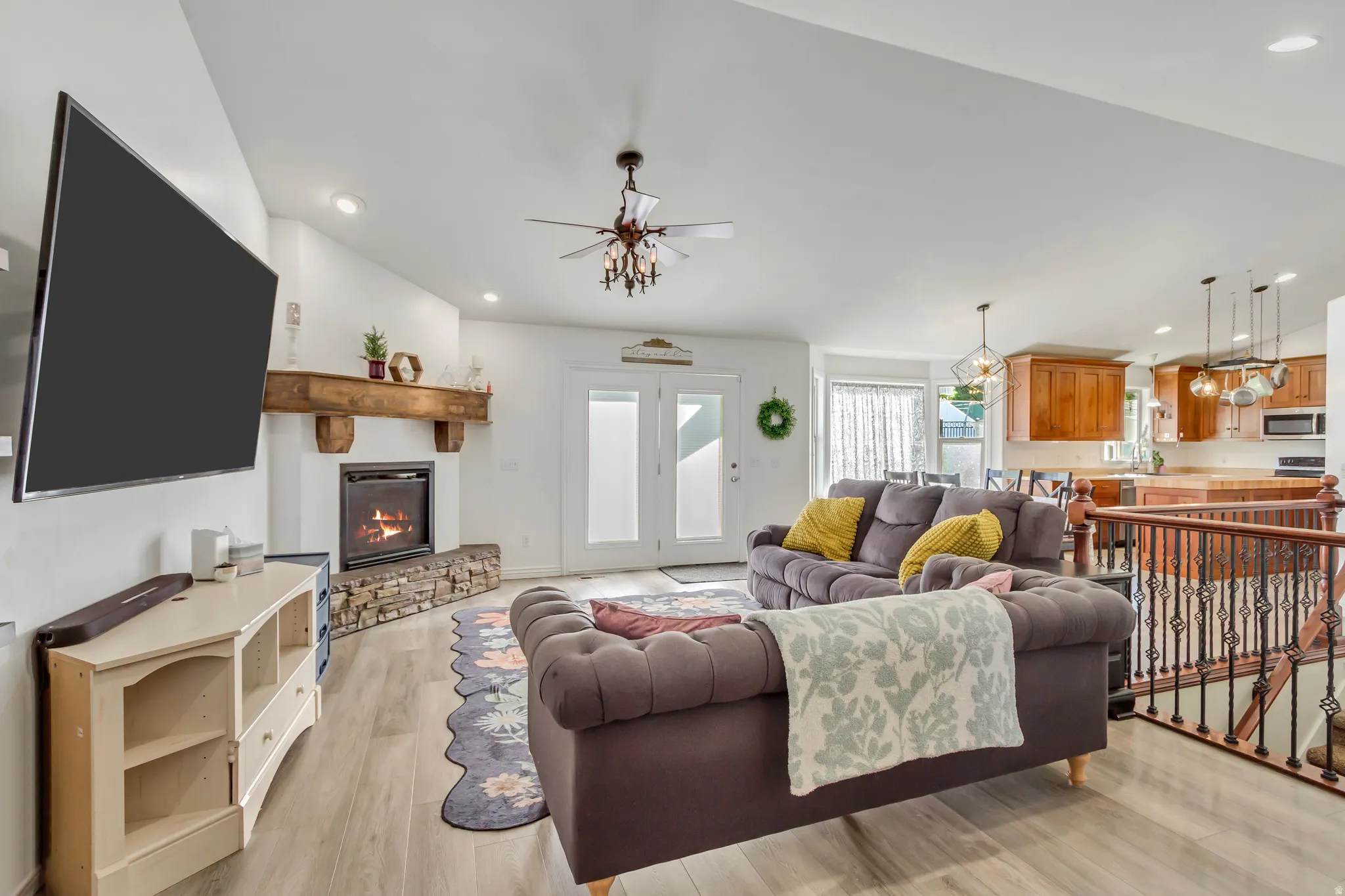 Spacious living area featuring a stone-faced fireplace with a wood mantel, wood-finish flooring, and a ceiling fan