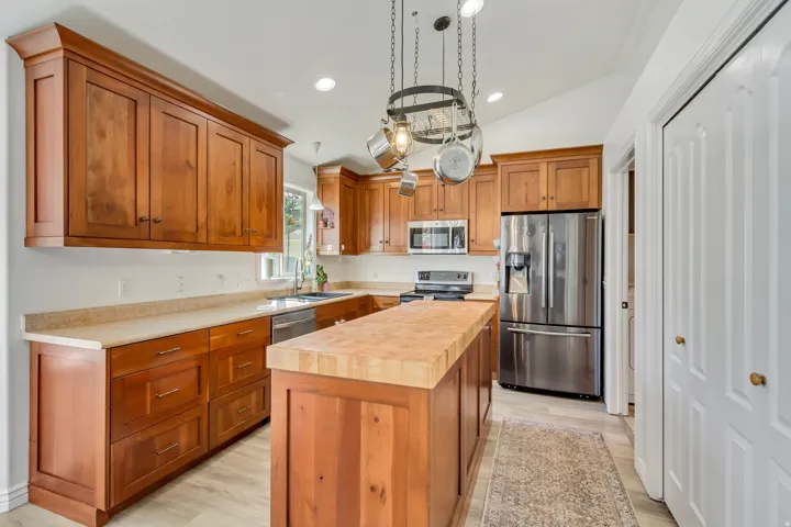 Kitchen featuring wood cabinetry, light-toned countertops, stainless steel appliances, a center island with a wood-finish top, and vaulted ceilings