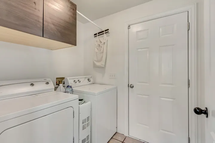 Laundry area featuring wood-finish upper cabinetry, a white panel door, and tile flooring