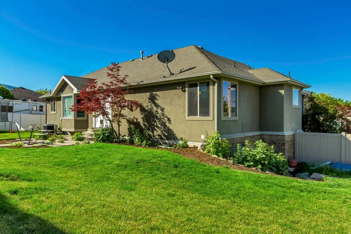 Exterior featuring stucco siding, a composition shingle roof, bay windows, and a landscaped yard with mature plantings