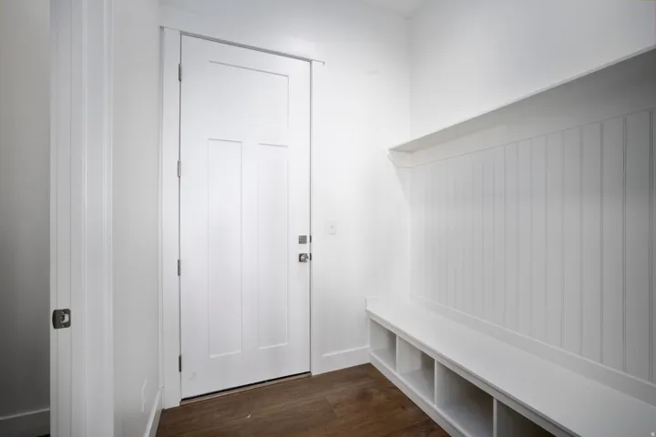 Entry area featuring white shaker-style door, wood-finish flooring, and built-in storage bench with cubbies
