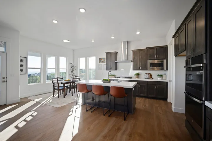 Modern kitchen and dining area featuring wood-finish flooring, recessed lighting, and ample natural light from multiple windows