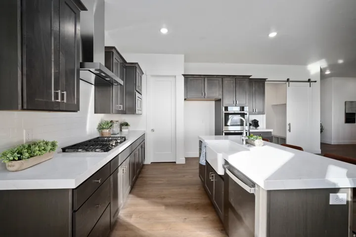 Contemporary kitchen featuring dark wood-finish cabinetry, light countertops, an island with an apron-front sink, and wood-finish flooring