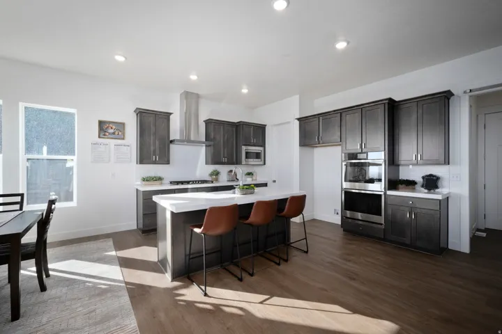 Kitchen featuring dark wood-finish cabinetry, stainless steel appliances, a center island with white countertop, and wood-finish flooring