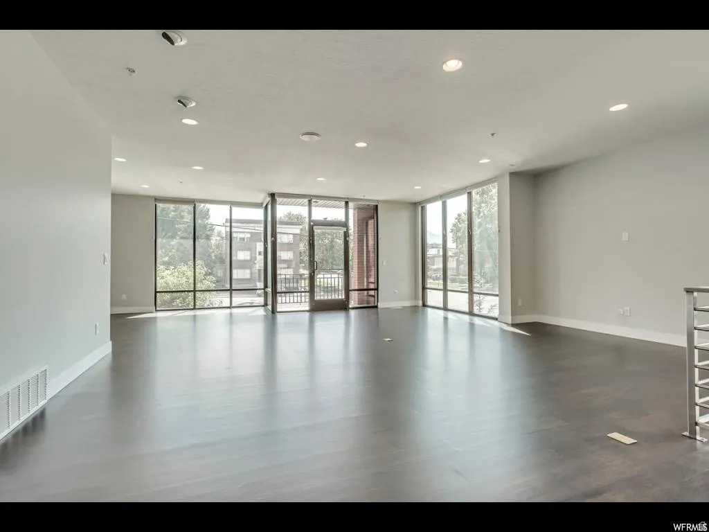 Expansive living area featuring wood-finish flooring, ample natural light through large windows, recessed ceiling lighting, and a neutral color palette