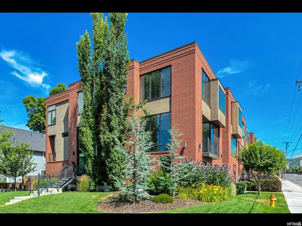 Modern brick exterior with expansive windows, multiple balconies, and a landscaped front lawn