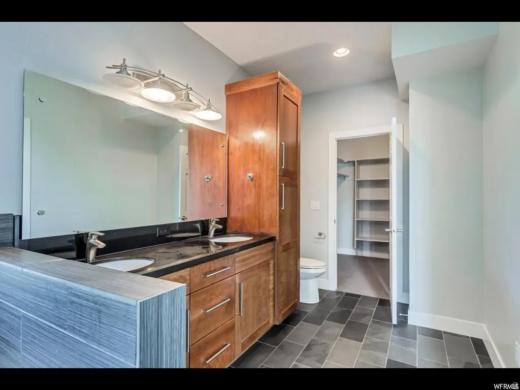 Dual vanity with undermount sinks and black countertop, complemented by a large wall-mounted mirror and brushed nickel light fixture