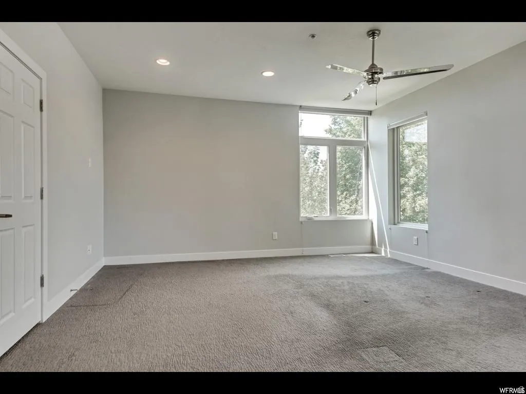 Spacious interior room featuring multiple large windows, recessed ceiling lighting, and a modern ceiling fan with metallic blades