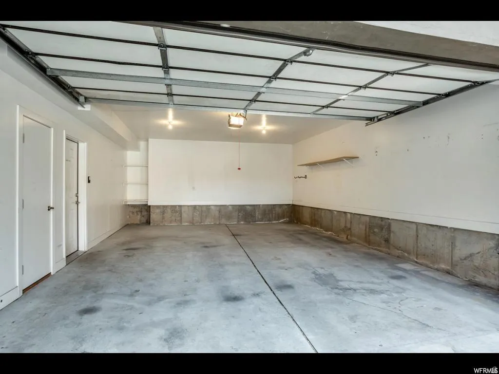 Spacious garage featuring a concrete floor, overhead lighting, an exposed garage door mechanism, built-in shelving, and two entry doors
