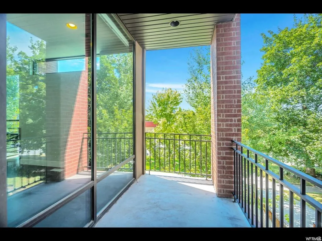 Private balcony featuring brick columns, black metal railings, a concrete floor, and ample natural light from surrounding foliage