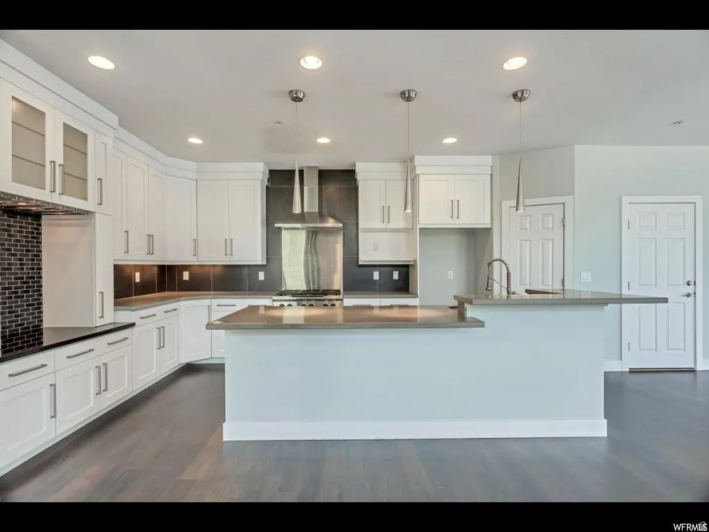 Contemporary kitchen featuring white cabinetry, a large island with a breakfast bar, and stainless steel appliances including a range hood