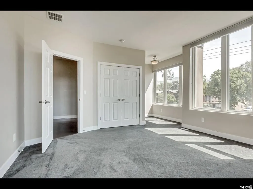 Spacious room featuring broad windows, light gray walls, plush gray carpeting, and white trim