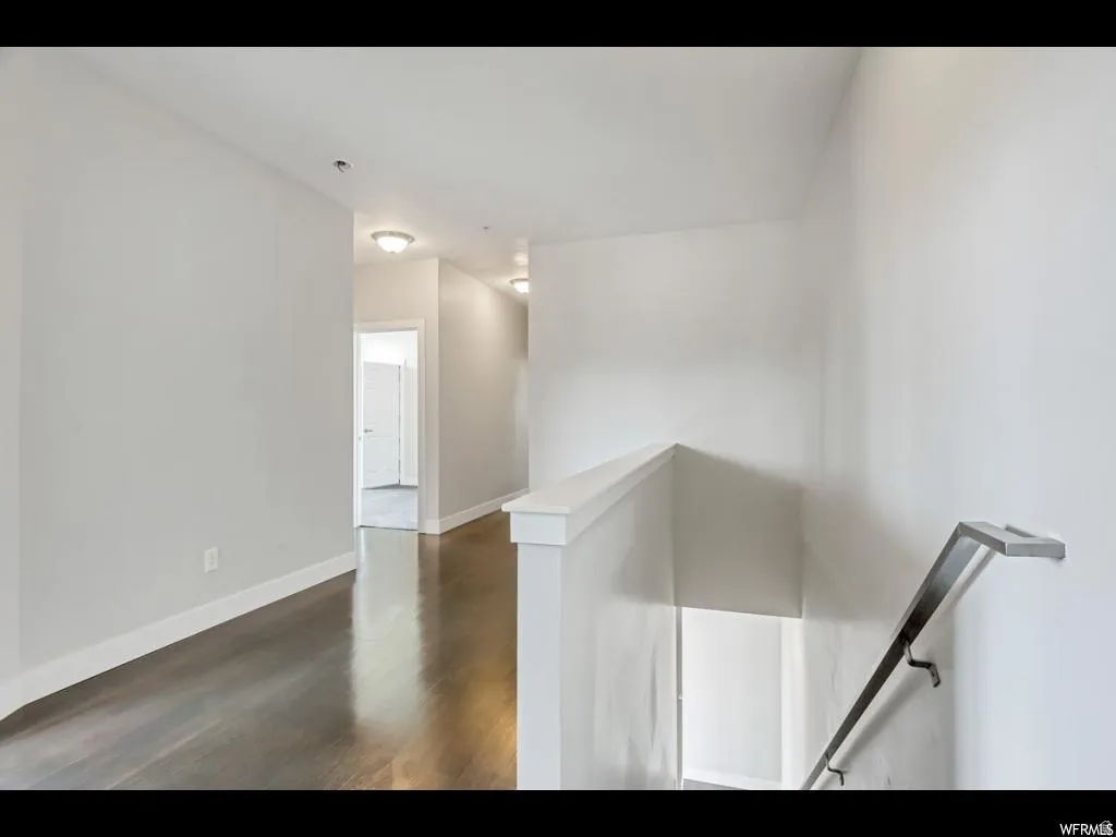 Hallway featuring dark wood-finish flooring, white baseboards, and light gray walls