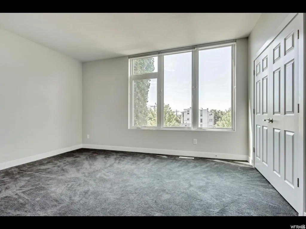 Spacious interior room featuring light gray walls, dark gray carpeting, and white baseboards