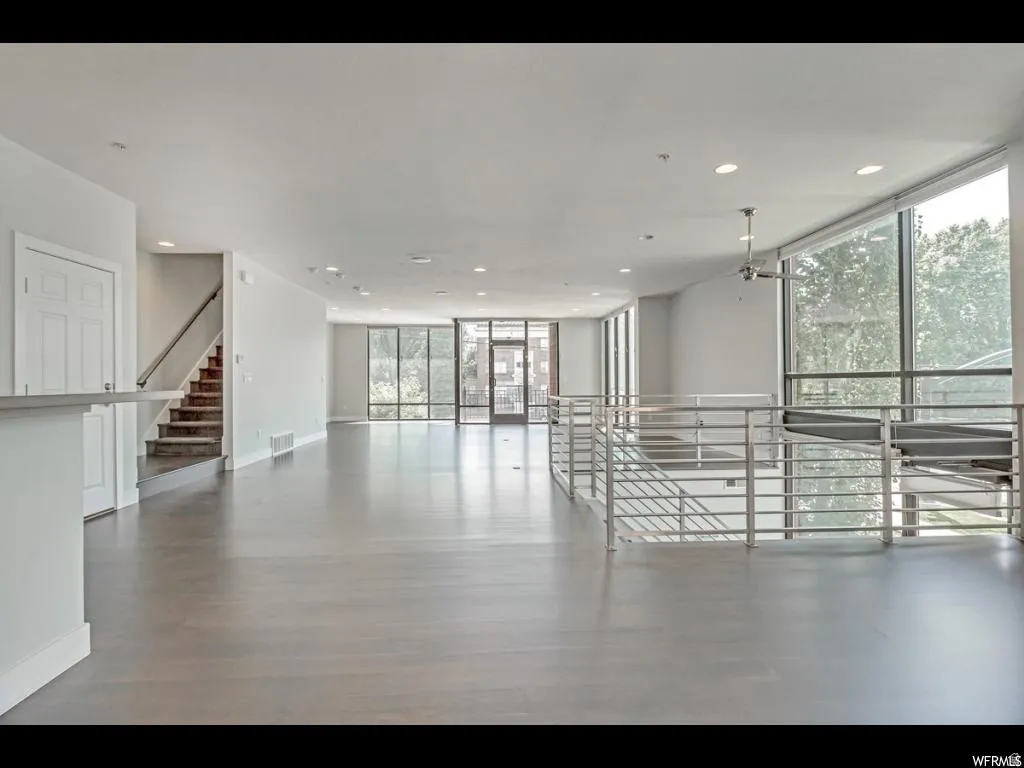 Open-concept living area featuring wood-finish flooring, a contemporary staircase with metal railings, and expansive floor-to-ceiling windows
