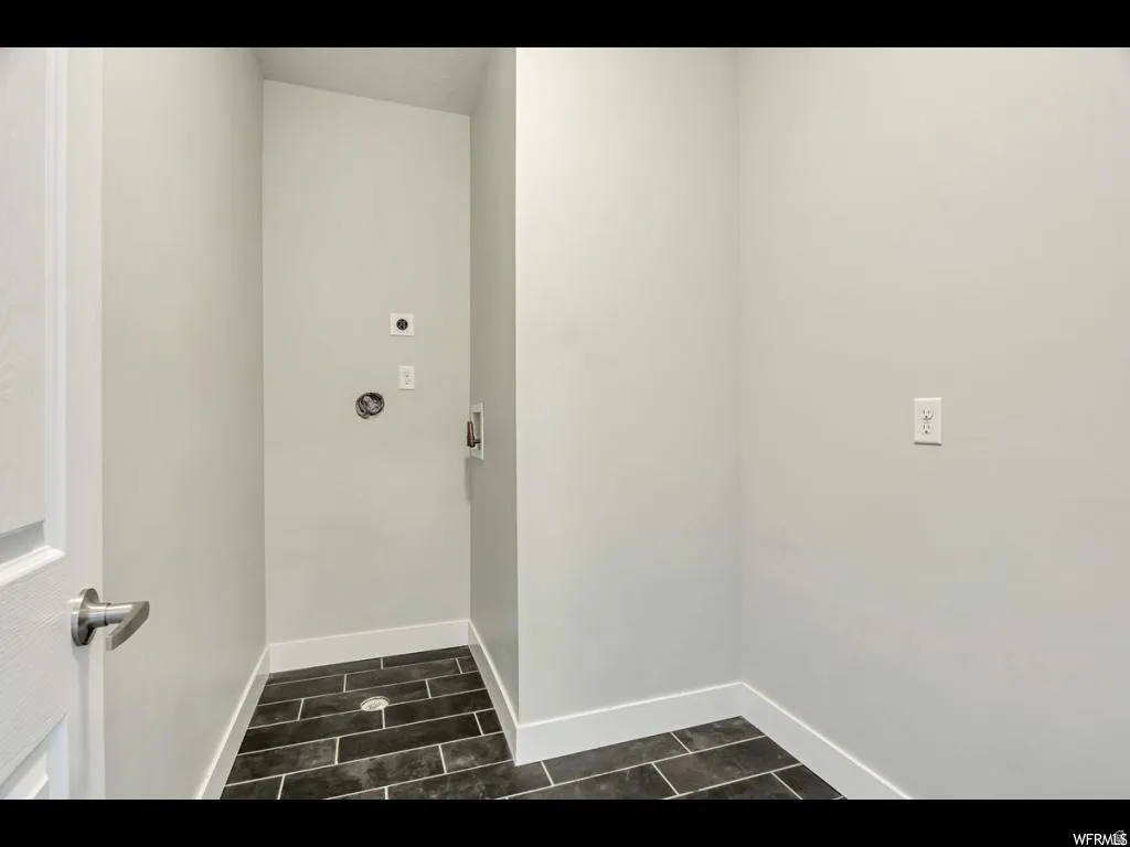 Dedicated utility space featuring dark rectangular floor tiles, light-toned walls, and white baseboards