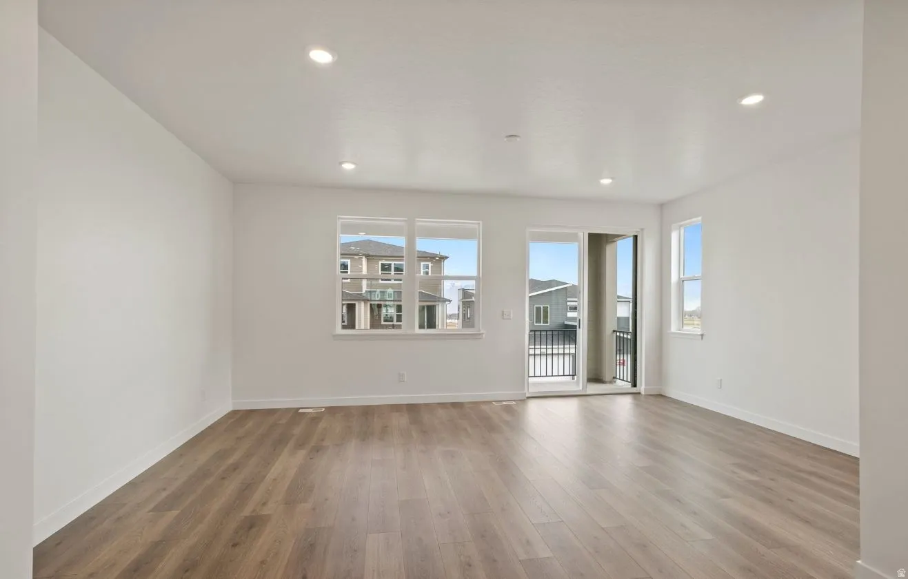 Spacious room featuring wood-finish flooring, white walls, recessed ceiling lighting, and large windows