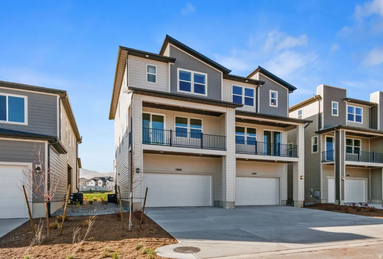 Modern multi-level townhome featuring a contemporary exterior with contrasting siding, dual balconies with black railings, multiple windows, and an integrated two-car garage