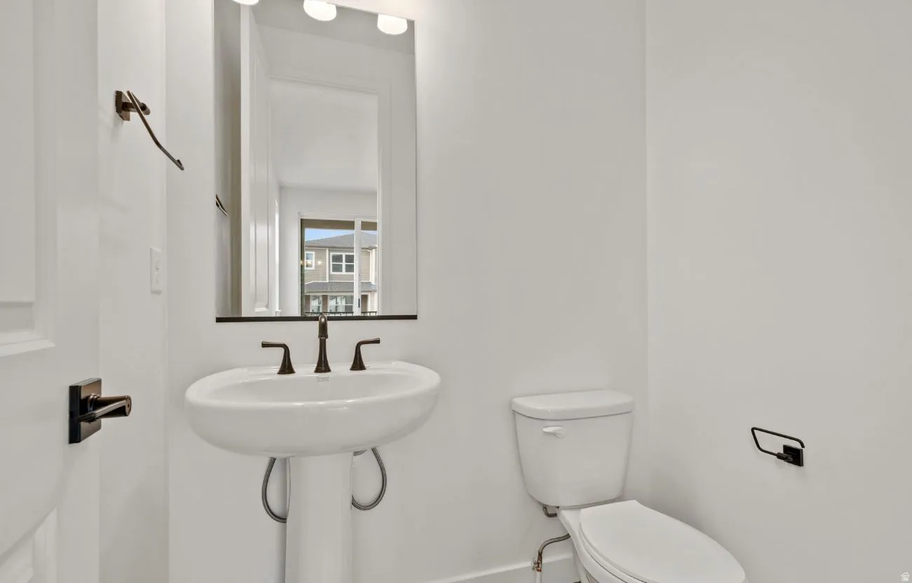 Pedestal sink with dark bronze fixtures, framed mirror, and integrated vanity lighting