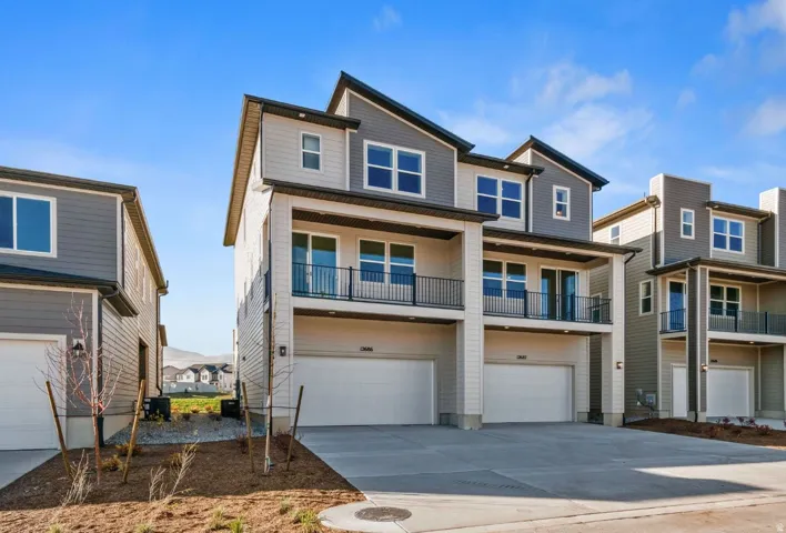 Modern multi-level townhome featuring a contemporary exterior with contrasting siding, dual balconies with black railings, multiple windows, and an integrated two-car garage