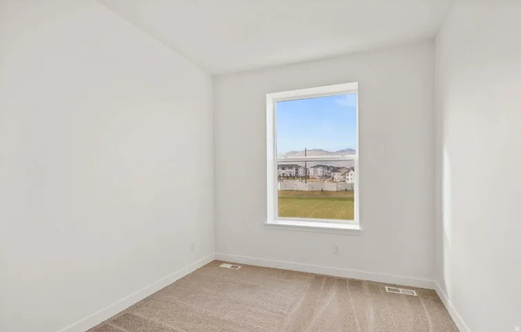Bright interior room featuring a large window, neutral carpeting, white baseboards, and white painted walls