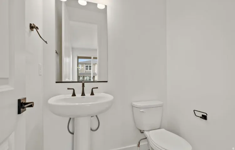Pedestal sink with dark bronze fixtures, framed mirror, and integrated vanity lighting