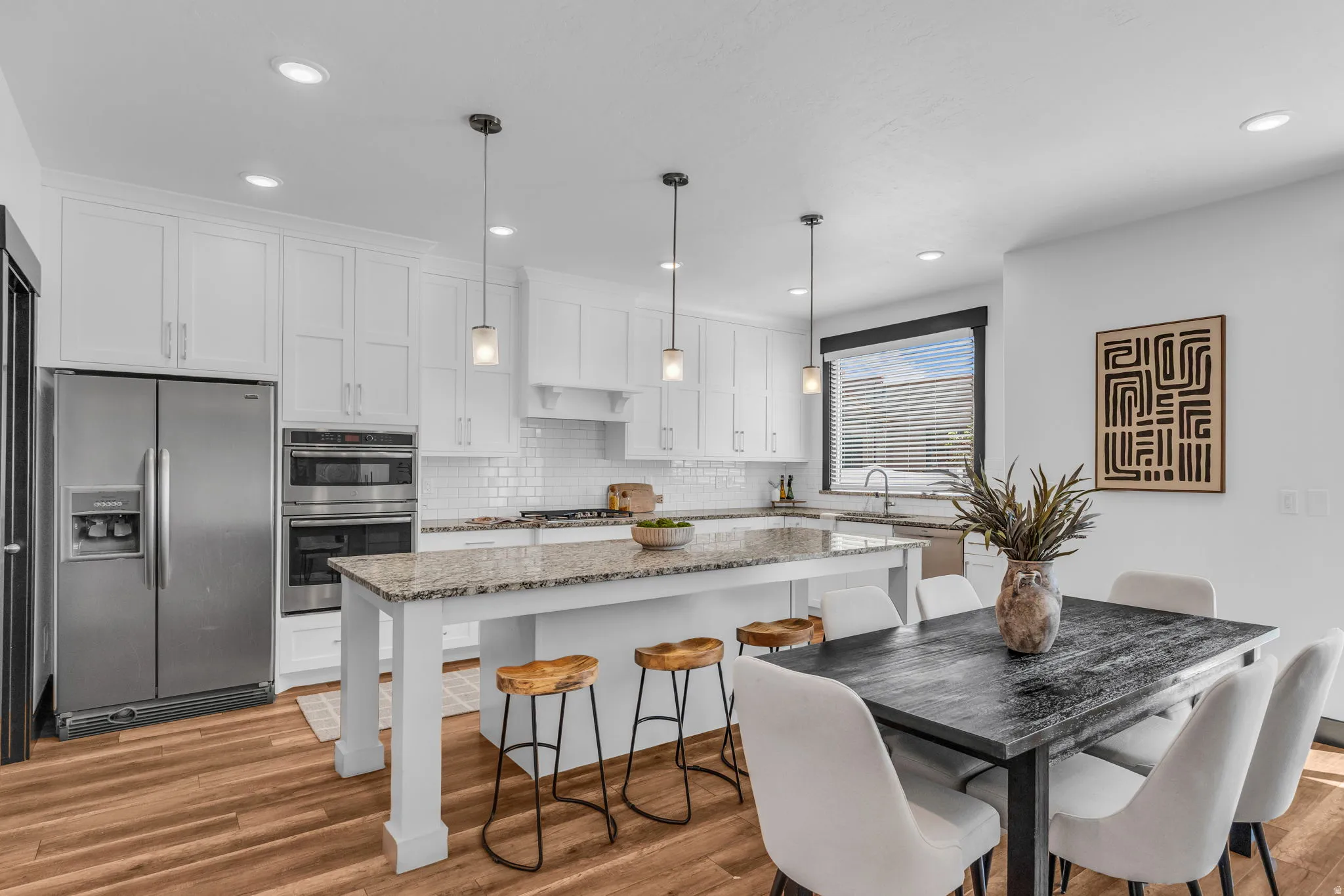 Open-concept kitchen and dining area featuring white cabinetry, subway tile backsplash, stainless steel appliances, granite countertops, and wood-finish flooring