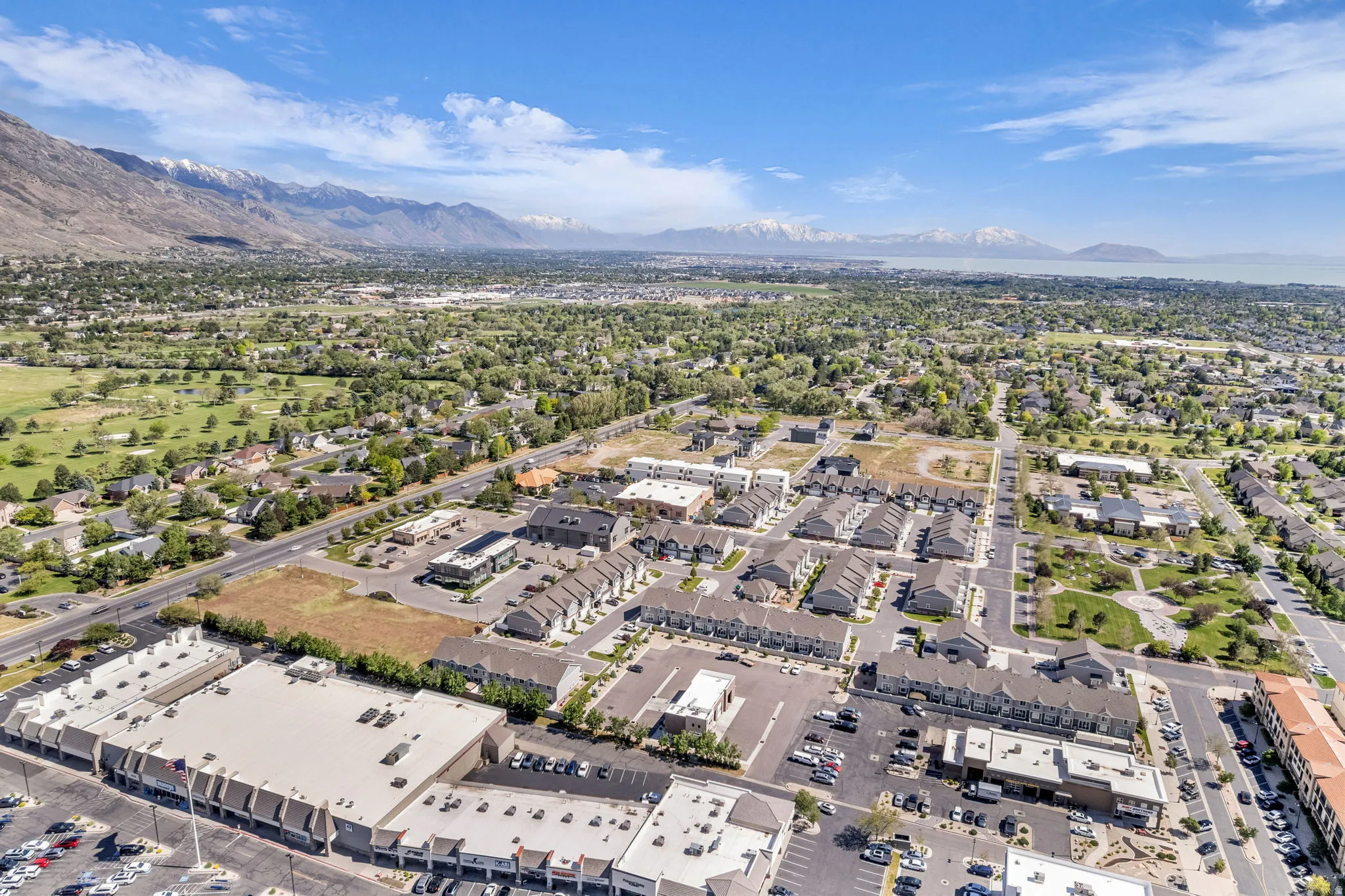 Aerial perspective showcasing a residential and commercial area with prominent mountain ranges and a large body of water in the distance