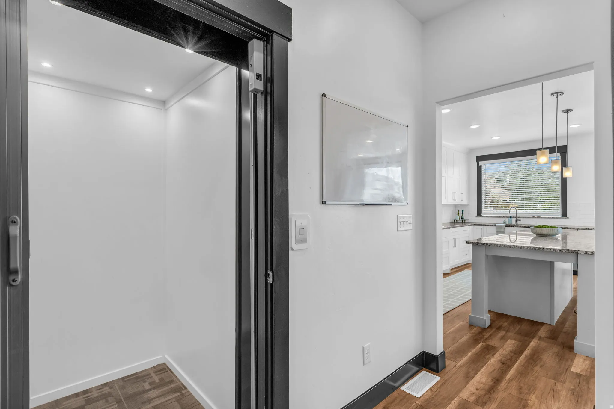 Open kitchen with a light granite island, white cabinetry, undermount sink, and dark-framed window