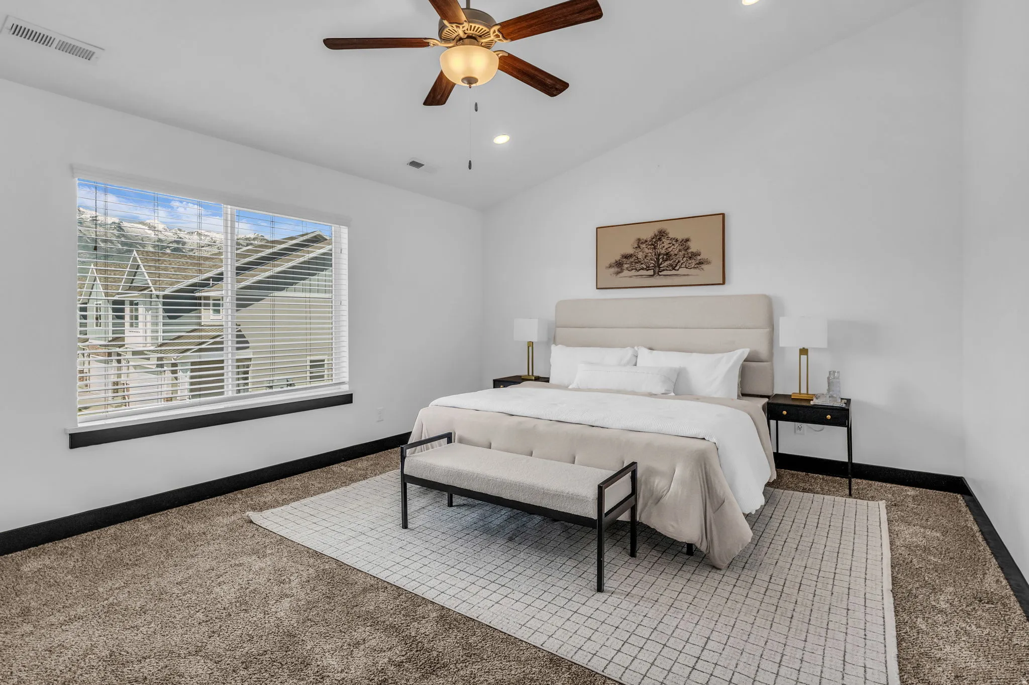Spacious bedroom featuring a vaulted ceiling with a ceiling fan, plush carpeting, a large window with horizontal blinds, and recessed lighting