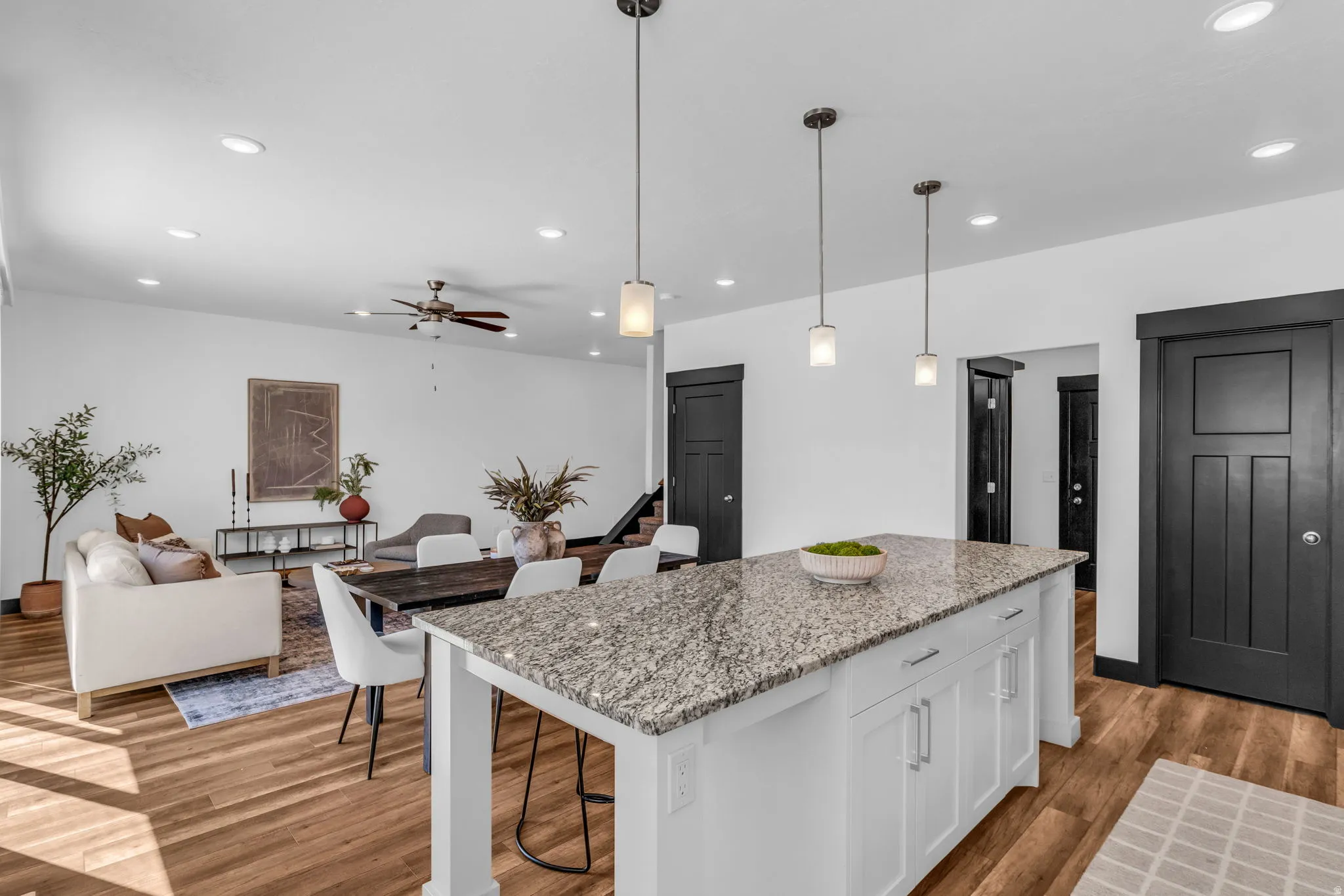 Central kitchen island with a granite countertop, white cabinetry, and pendant lighting