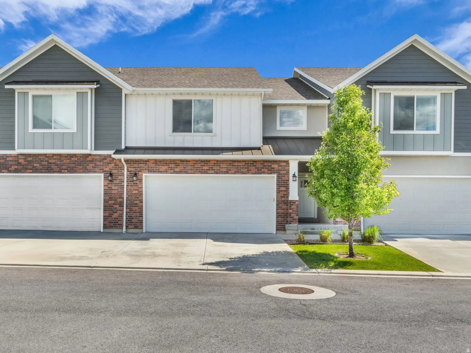 Modern townhome exterior featuring a combination of brick and siding, multiple attached garages, concrete driveways, and a manicured lawn with mature trees