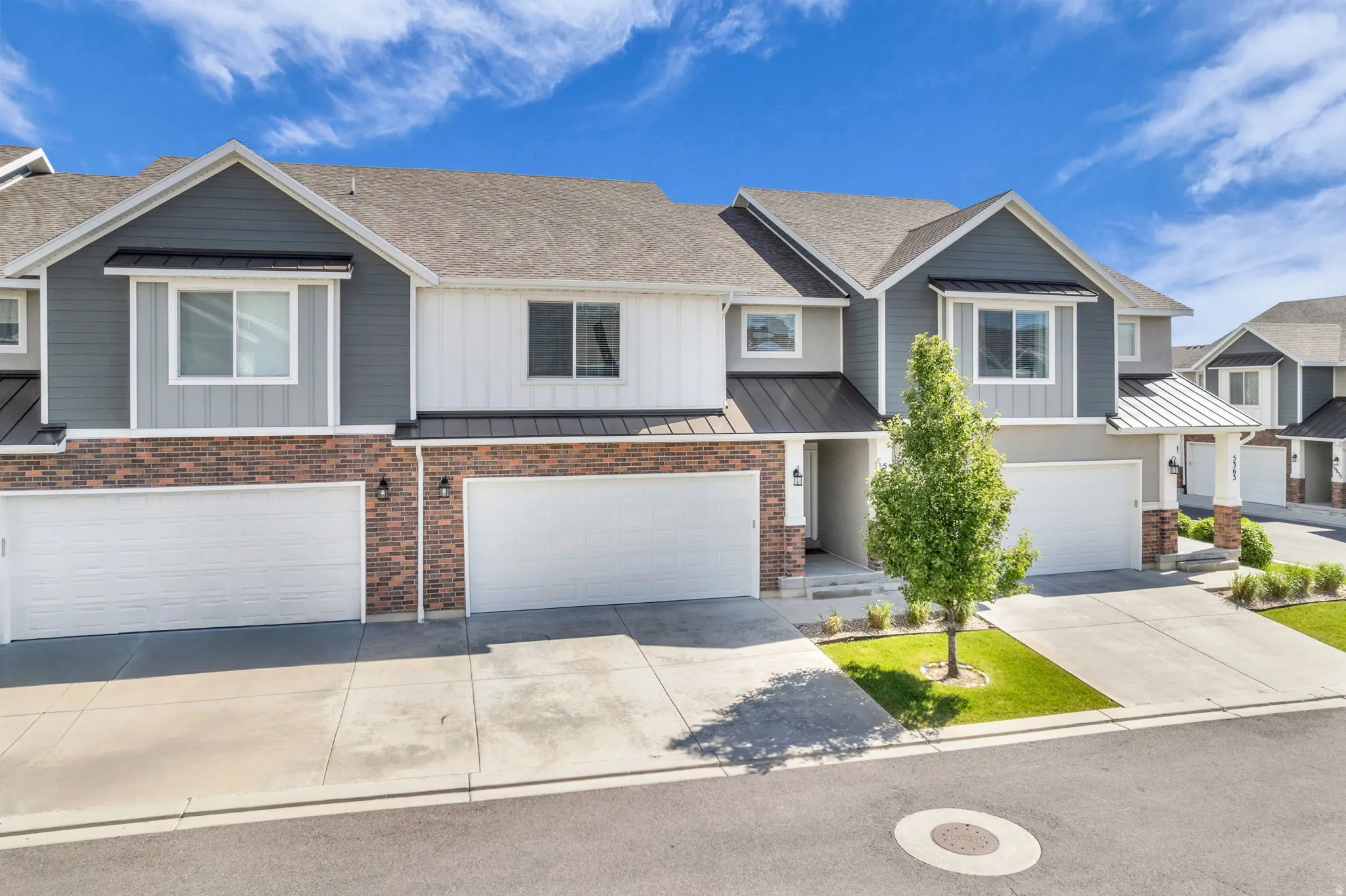 Modern townhome facade featuring a blend of brick and siding, two-car garage, covered entry, and manicured landscaping