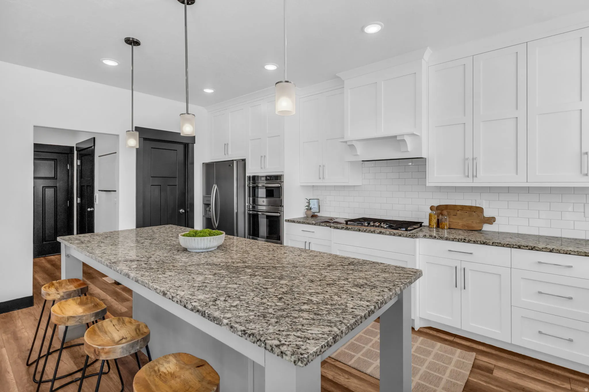 Kitchen featuring a large island with a stone countertop, white shaker cabinetry, stainless steel appliances, and wood-finish flooring