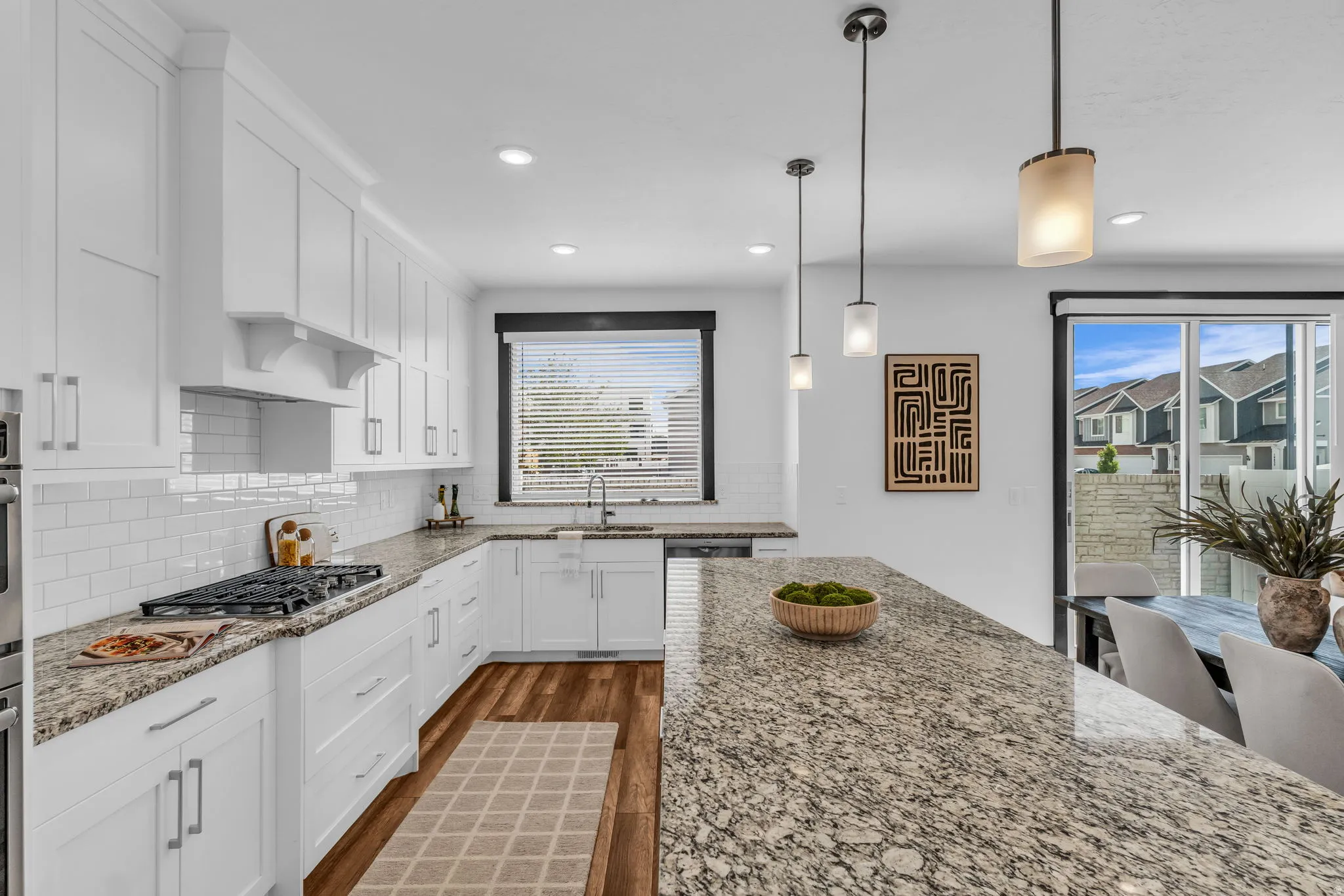 Open-concept kitchen featuring an expansive granite countertop island, white shaker cabinetry, stainless steel appliances, and wood-finish flooring