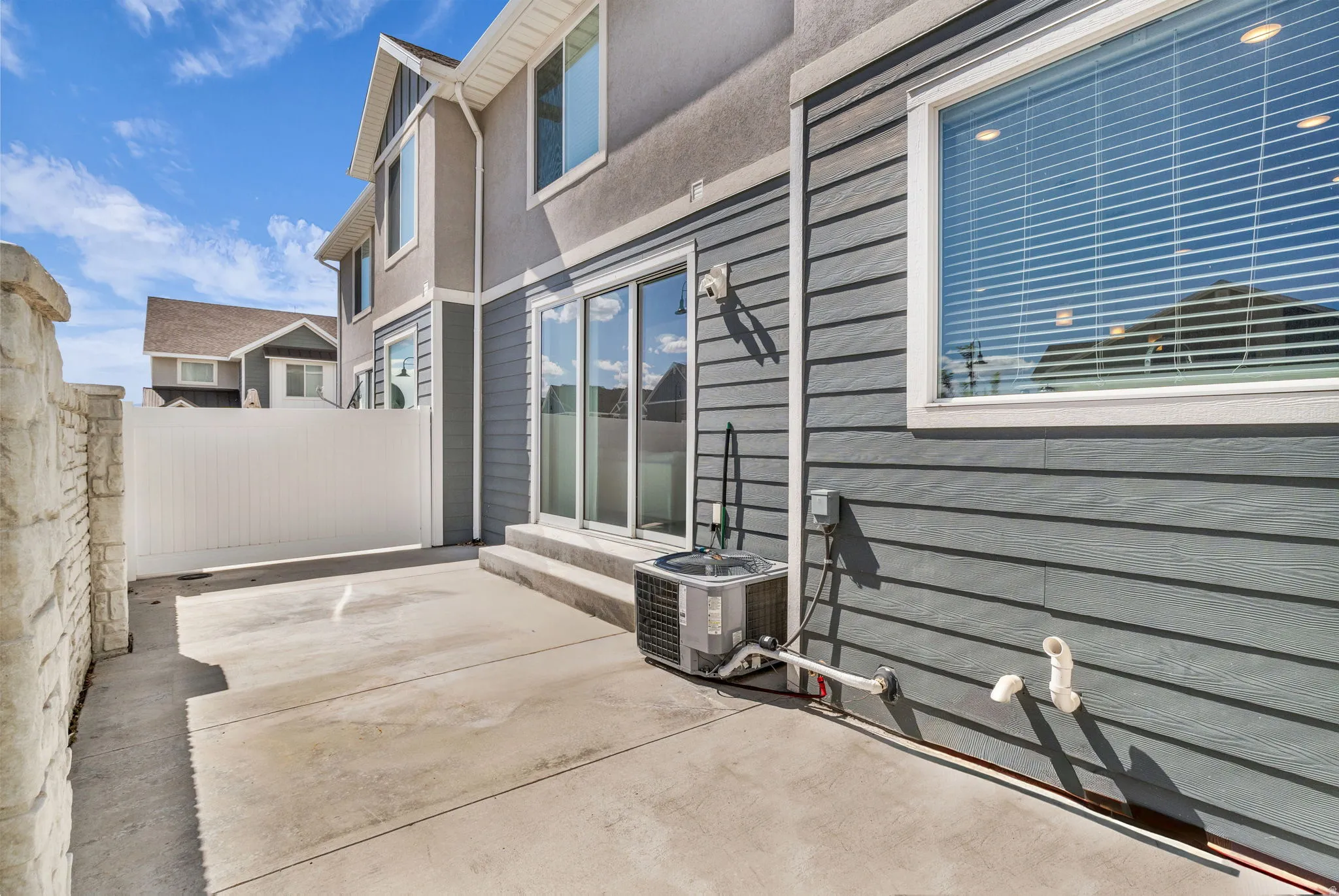 Concrete patio area featuring a stone-faced privacy wall, white vinyl fencing, and a multi-pane glass sliding door