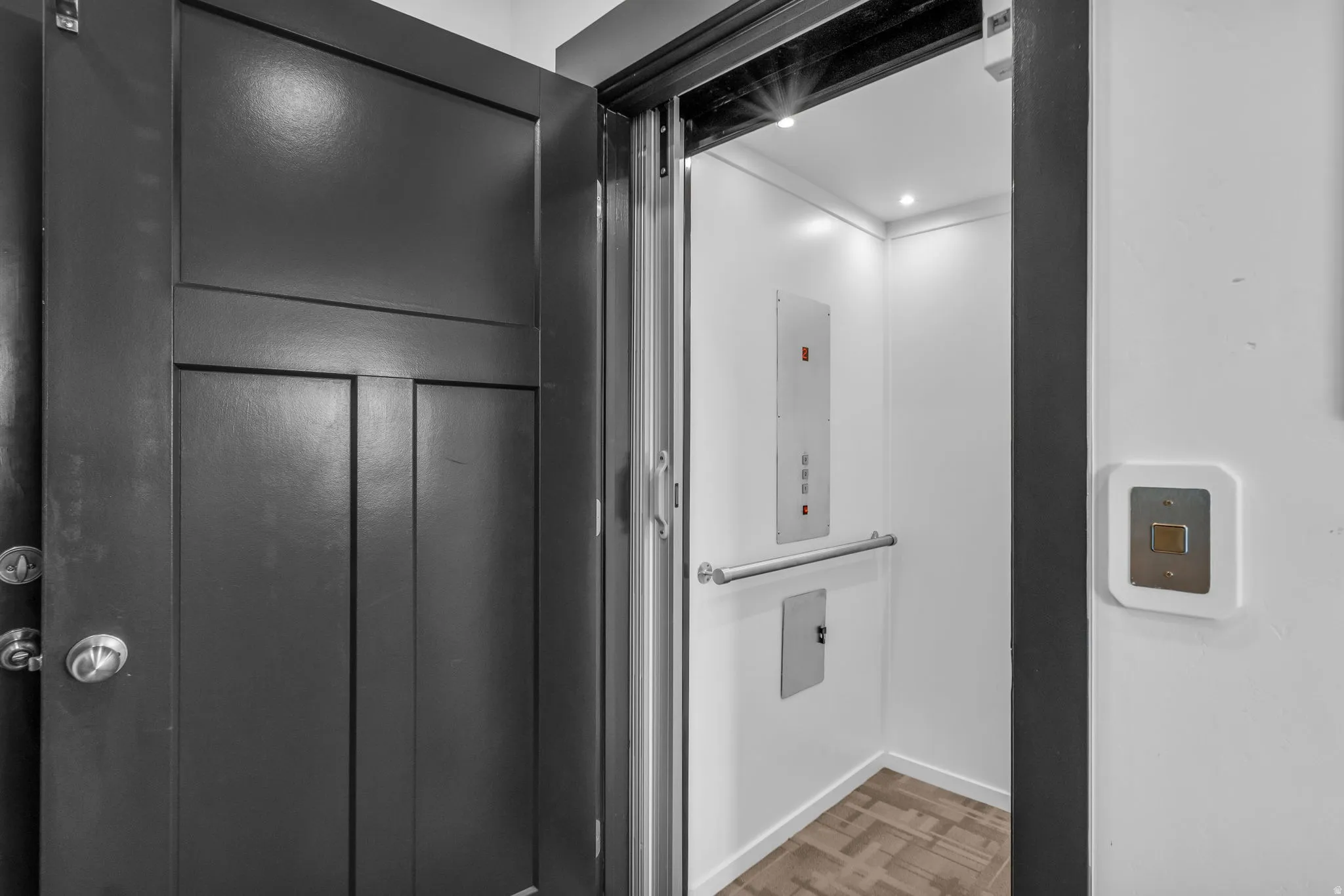 Private elevator with a clean white interior, recessed lighting, a stainless steel handrail, and wood-finish flooring