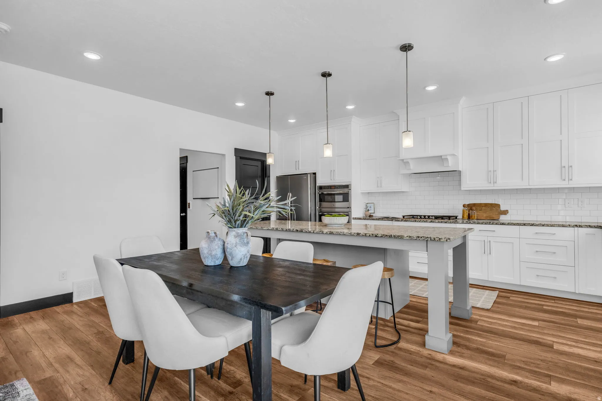 Spacious open-concept kitchen and dining area featuring wood-finish flooring, white shaker cabinetry, an island with seating, a subway tile backsplash, and recessed and pendant lighting