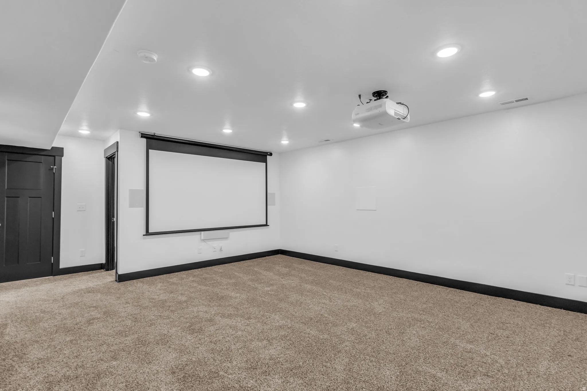 Dedicated media room featuring a large projection screen, ceiling-mounted projector, recessed lighting, and integrated wall speakers