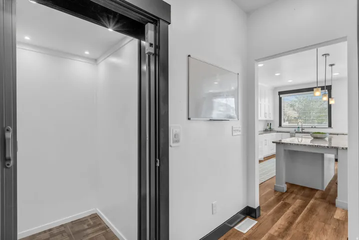 Open kitchen with a light granite island, white cabinetry, undermount sink, and dark-framed window