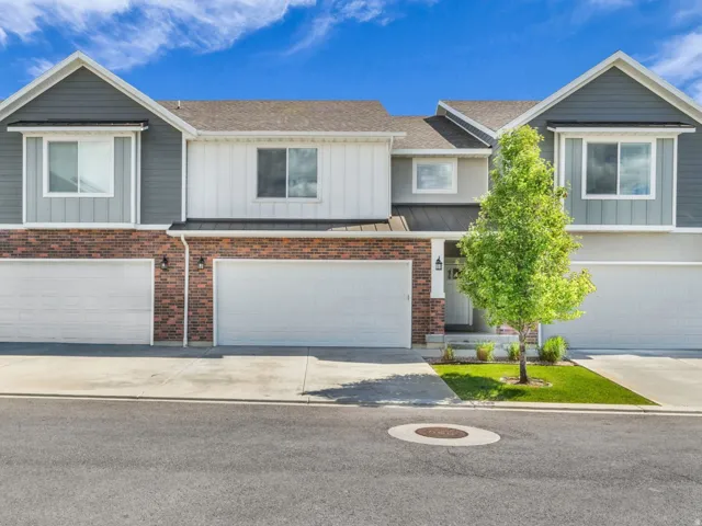 Modern townhome exterior featuring a combination of brick and siding, multiple attached garages, concrete driveways, and a manicured lawn with mature trees