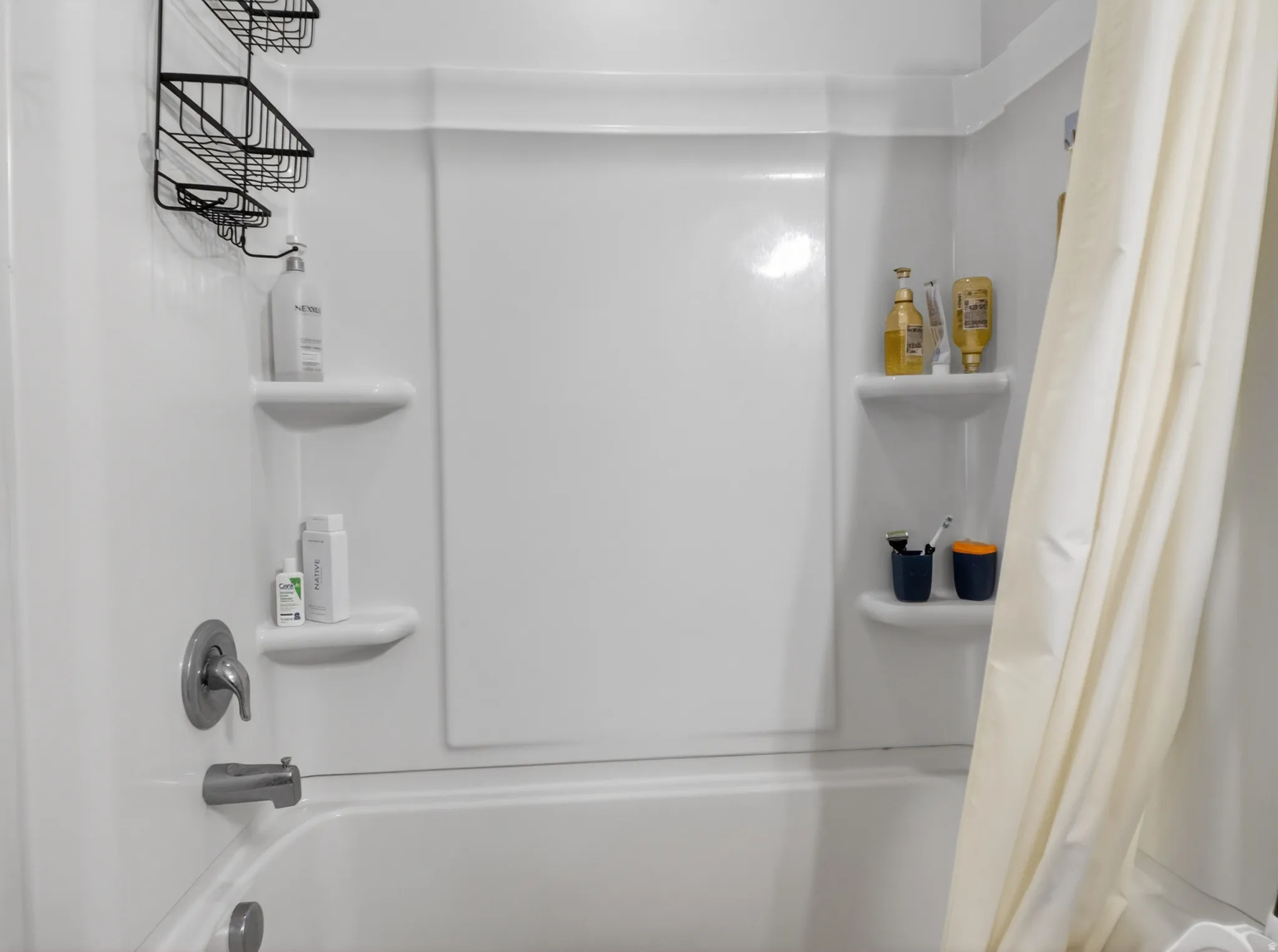 White fiberglass tub and shower combination featuring integrated corner shelving and a chrome tub filler with single-handle control