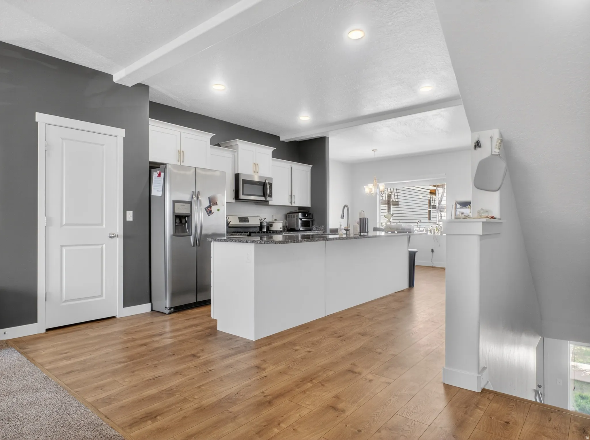 Open-concept kitchen featuring an island with a sink, stainless steel appliances, white cabinetry with gold-tone hardware, and wood-finish flooring