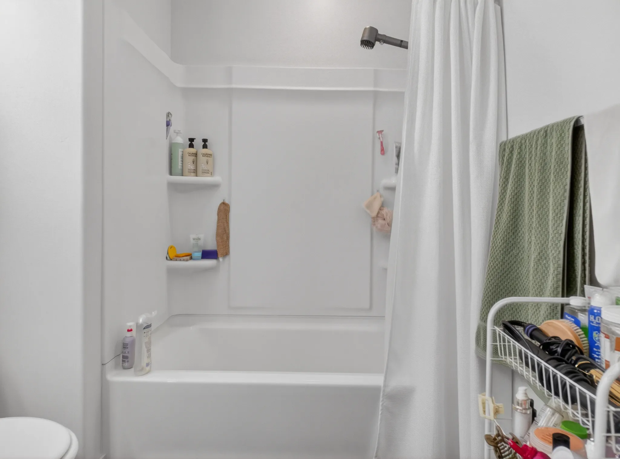 White fiberglass tub and shower combination with integrated shelving, matte black showerhead, and white shower curtain rod