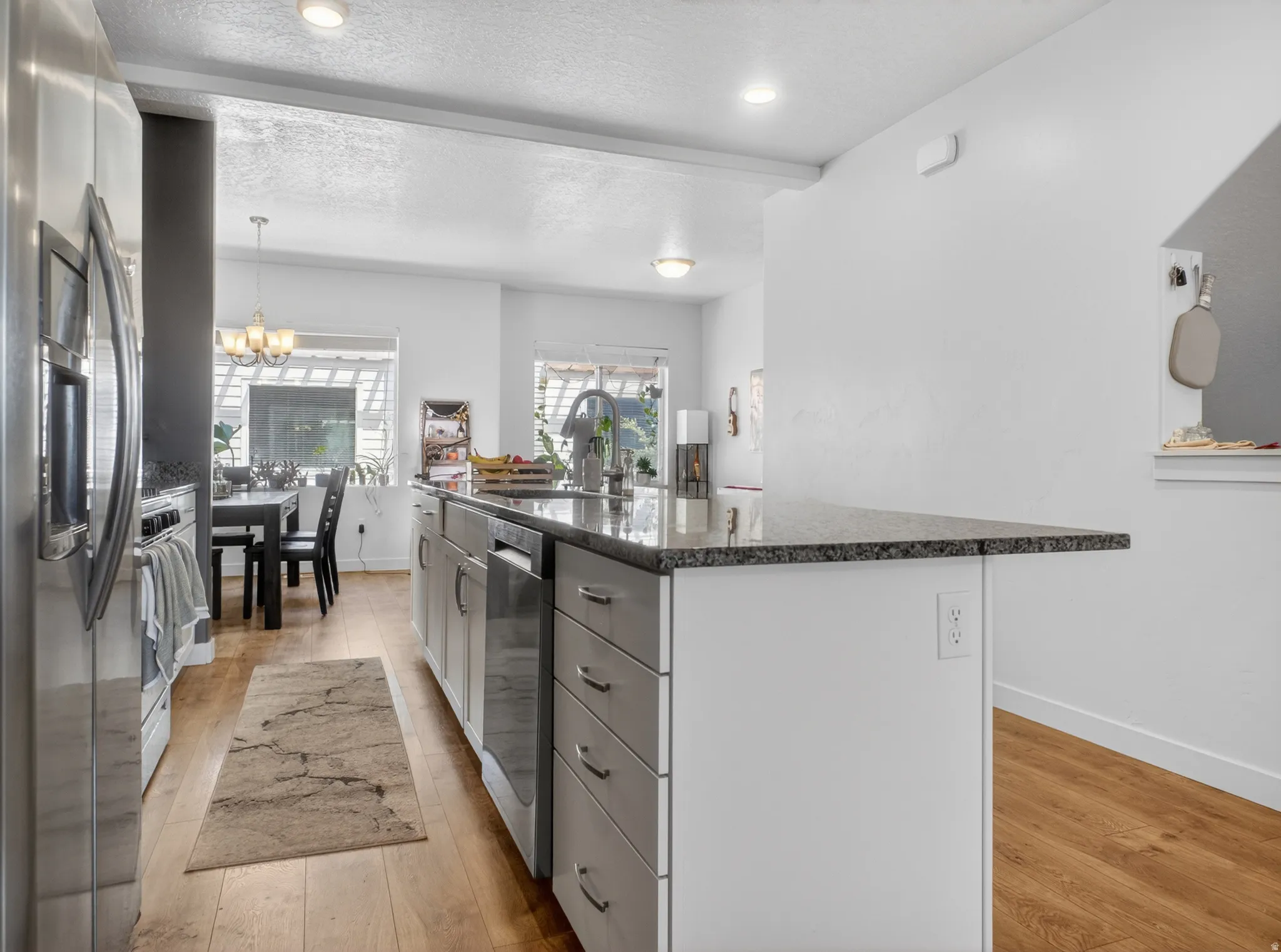 Spacious kitchen featuring a large island with a stone-finish countertop, stainless steel appliances, wood-finish flooring, recessed lighting, and white cabinetry
