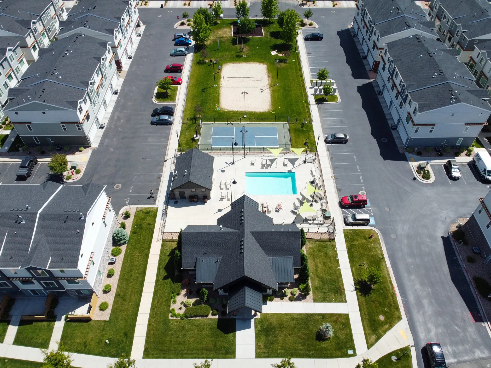 Aerial view showcasing community amenities including a swimming pool with ample lounge seating, a tennis court, and a volleyball court