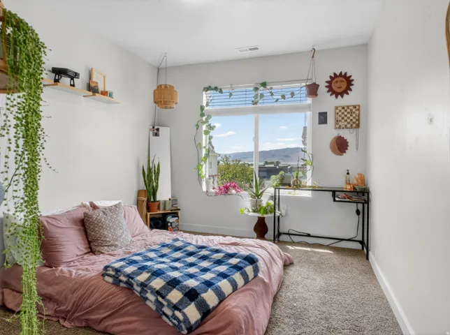 Bright bedroom featuring a large window with horizontal blinds, neutral wall paint, and plush carpet flooring