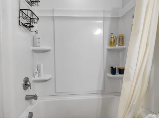 White fiberglass tub and shower combination featuring integrated corner shelving and a chrome tub filler with single-handle control