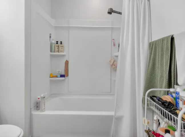 White fiberglass tub and shower combination with integrated shelving, matte black showerhead, and white shower curtain rod